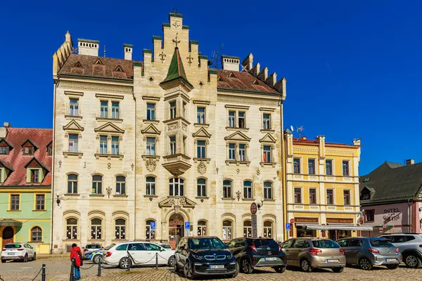 Güneşli kasaba meydanında park etmiş arabalarla tarihi gotik canlandırma mimarisi. 18 Mart 2025, Madalyon, Çek Cumhuriyeti.