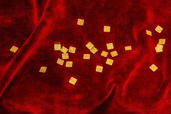 Lüks kırmızı kadife kumaş arka planda dağınık altın sikkeler. 18 Mart 2025, Madalyon, Çek Cumhuriyeti.