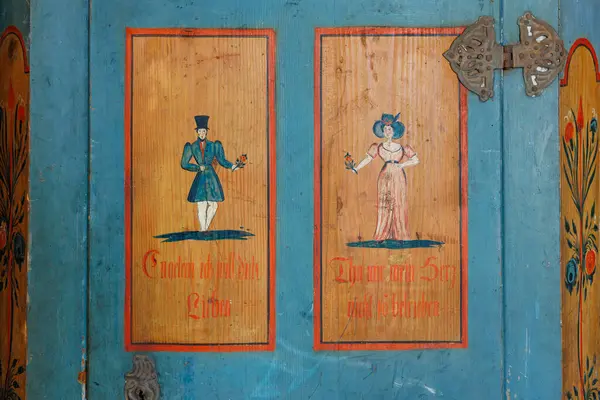 Mavi ahşap dolapta erkek ve kadın figürleri olan klasik halk sanatı panelleri. 18 Mart 2025, Madalyon, Çek Cumhuriyeti.