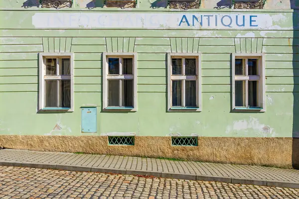 Yaşlanmış yeşil bina dış tarafında, kaldırım taşı sokağında yıpranmış antika tabelaları var. 18 Mart 2025, Madalyon, Çek Cumhuriyeti.