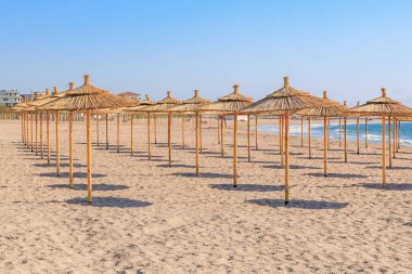 Okyanus kenarında güneşli bir günde saman şemsiyeli boş bir sahil..