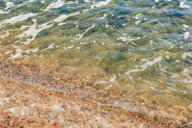 Kayalık kıyı şeridinde güneşli berrak sularda hafif dalgalar.