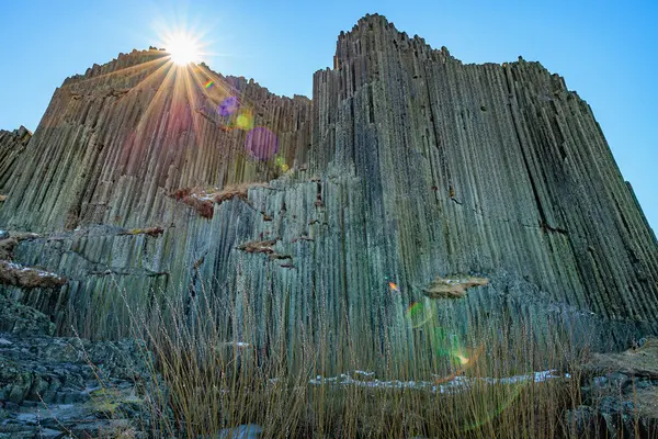 Güneşli bazalt sütunlar ve açık gökyüzünün altında çimenler.