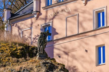 Pembe bina Nikolina 'nın yanında haç tutan kadın heykeli. 19 Mart 2025, Karlovy Vary, Çek Cumhuriyeti.