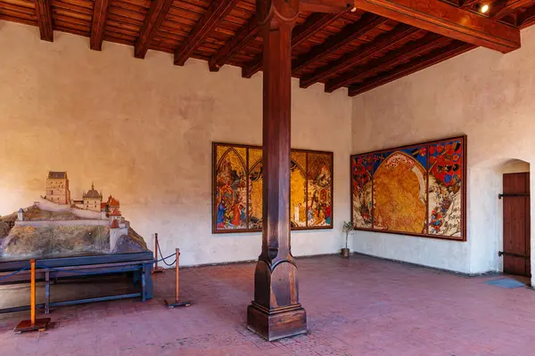 Ortaçağ şatosunun içinde ahşap sütun ve detaylı duvar halısı sanat eserleri var. 19 Mart 2025, Karlstejn, Çek Cumhuriyeti.