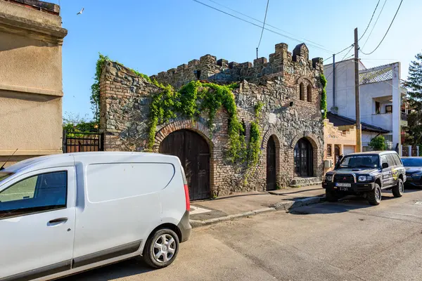 Sarmaşık kaplı duvarları ve şehir caddesinde kemerli pencereleri olan taş bir ev. 4 Mayıs 2025 Romanya.