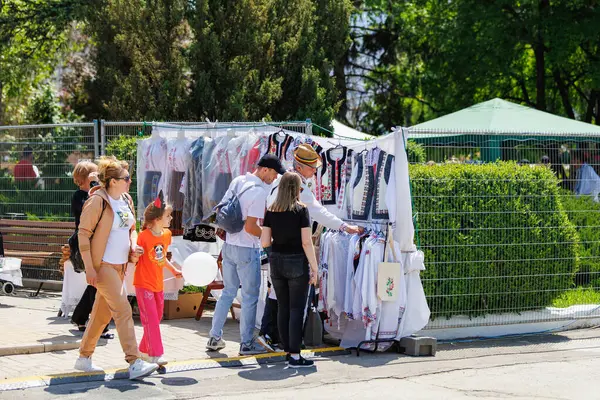 İnsanlar güneşli bir günde geleneksel kıyafet sergisiyle açık hava pazarından alışveriş yapıyorlar. 22 Mayıs 2025 Balti Moldova.