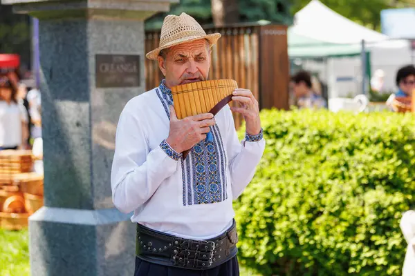 Geleneksel kıyafetlerle dışarıda pan flütü çalan yaşlı beyaz bir erkek. 22 Mayıs 2025 Balti Moldova.