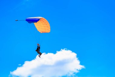 Açık mavi gökyüzüne karşı turuncu ve mavi paraşütlü genç erkek paraşütçü. 31 Mayıs 2025 Vadul lui Voda Moldova.