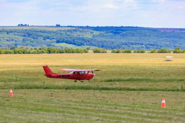 Manzaranın ve yuvarlanan tepelerin ortasında çimen pistinde küçük kırmızı bir uçak. 31 Mayıs 2025 Vadul lui Voda Moldova.