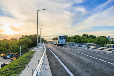 Gün batımında, yemyeşil manzaralı kırsal yolda otobüs köprüden geçiyor. 2 Haziran 2025 Balti Moldova.