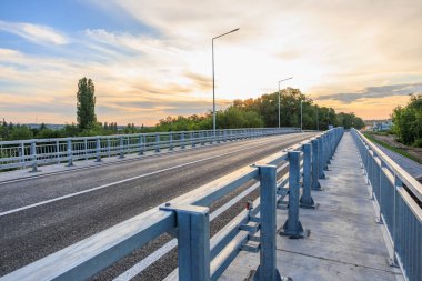 Gün batımında yeşil manzarada parmaklıkları olan boş bir yol köprüsü. 2 Haziran 2025 Balti Moldova.
