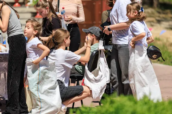 Enerjik beyaz çocuklar yetişkinlerle açık hava çuval yarışı yapıyor. 22 Mayıs 2025 Balti Moldova.