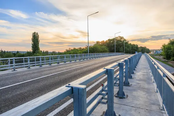 Gün batımında yeşil manzarada parmaklıkları olan boş bir yol köprüsü. 2 Haziran 2025 Balti Moldova.