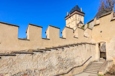 Temiz mavi gökyüzünün altında tarihi kale kulesi ve taş duvar.