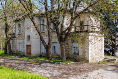 Güneşli bir günde ağaçlarla çevrili eski taş bir ev..