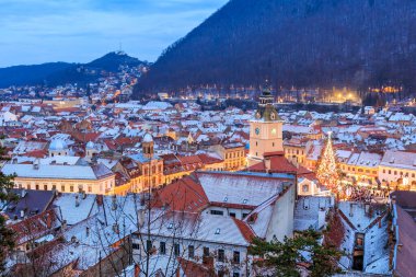 Geceleri ortasında Noel ağacı olan bir şehir. Şehir ışıklarla aydınlanıyor ve gökyüzü bulutlu.