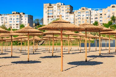 Güneşli bir günde saman şemsiyeli ve apartmanlı boş bir sahil..