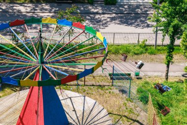 Açık hava parkında ağaçlar ve yürüyüş yollarıyla dolu renkli terk edilmiş bir atlıkarınca..