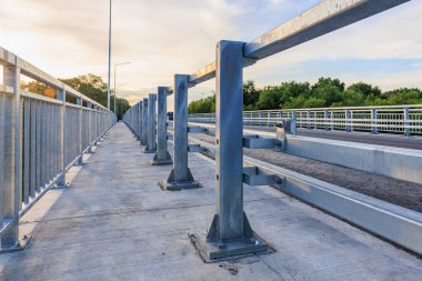 Günbatımında beton yolu ve parmaklıkları olan modern çelik köprü..