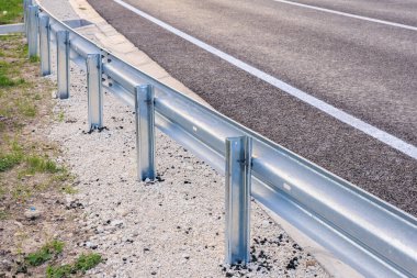 Araç güvenliği için asfalt yol boyunca eğri metal bariyerler.
