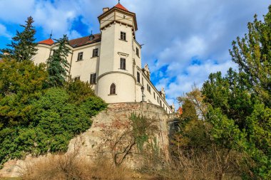 Mavi gökyüzünün altındaki yemyeşil ormanlarla çevrili tarihi Avrupa kalesi.