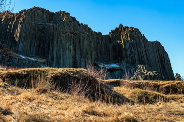 Doğal ortamda açık mavi gökyüzünün altında görkemli bazalt sütunlar.