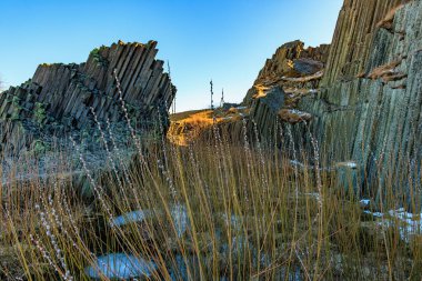 Güneş ışığında çimenli görkemli bazalt kaya oluşumları.