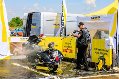 Bir motorcu, motosikletini dışarıdaki temizlik kabininde temizlemek için güçlü bir basınç makinası kullanır. Etkili araç temizleme ürünleri gösteriliyor. 2 Temmuz 2023 Liadoveni Moldova.