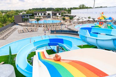 Üzerinde gökkuşağı olan renkli bir kaydırak bir su parkında. Kaydırak bir havuz ve diğer su çekimleri ile çevrilidir. 8 Haziran 2024 Balti Moldova