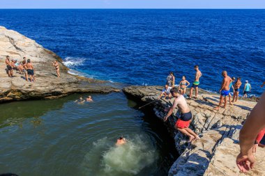 Bir grup insan arka planda mavi bir okyanus olan bir havuzda yüzüyorlar. Sahne canlı ve eğlenceli, çünkü insanlar suda eğleniyorlar. 6 Ağustos 2024 Giola Thassos Yunanistan.