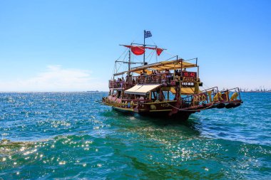 Kırmızı yelkenli ve beyaz tenteli büyük bir tekne okyanusta yüzüyor. Tekne insan kaynıyor ve teknede birkaç bayrak var. 8 Ağustos 2024 Selanik Yunanistan