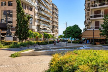 Ortasında çeşme olan bir şehir caddesi ve solunda bir adamın heykeli. Sokak binalar ve ağaçlarla dolu. 8 Ağustos 2024 Selanik Yunanistan