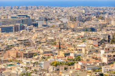 Arka planda büyük bir su kütlesi olan bir şehir manzarası. Şehir yüksek binalarla dolu ve etrafta dolaşan bir sürü insan var. Sahne meşgul ve hareketli. 9 Ağustos 2024 Atina Yunanistan