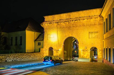 Büyük bir kemer yolu olan bir binanın önünde bir araba park edilmiş. Kemerler ışıklarla aydınlatılıyor, sıcak ve davetkar bir atmosfer yaratıyor. 13 Aralık 2024 Brasov Romanya