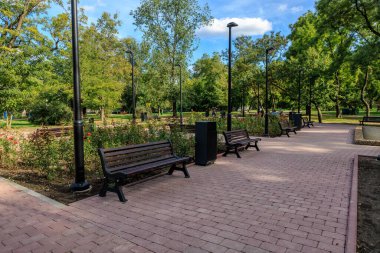 Tuğladan geçitli ve birkaç banklı bir park. Banklar sıraya dizildi, bazıları yaya yoluna dönük olacak. Park ağaçlarla çevrili. 25 Eylül 2024 Balti Moldova