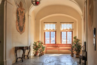 Güneşli koridor, tarihi binada saksı bitkileri ve dekoratif duvar dekorlarıyla dolu. 20 Mart 2025, Cesky Krumlov, Çek.