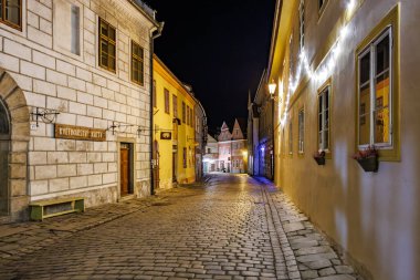 Gece vakti tarihi kaldırım taşı caddesinin aydınlık binalarla manzarası. 20 Mart 2025, Cesky Krumlov, Çek.
