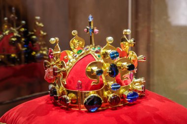 Altın taç, kadife yastıkta renkli taşlar sergileniyor..