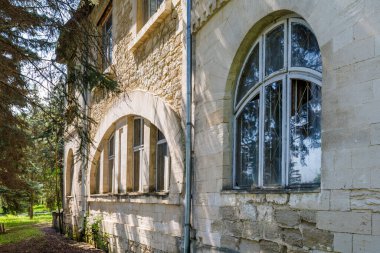Rustic stone architecture of abandoned building with arched windows in sunlit forest.