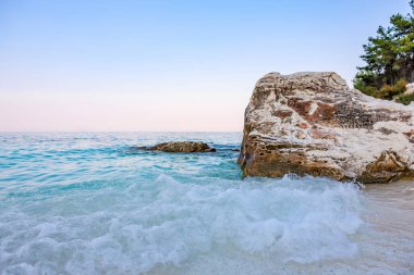 Kıyıya yakın okyanusta büyük bir kaya var. Su sakin ve gökyüzü mavi.