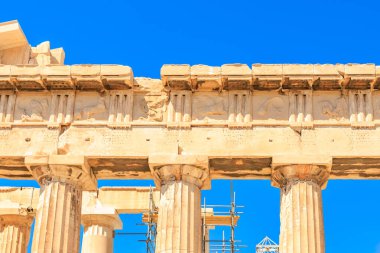 Sütunlar taştan yapılmıştır ve bir binanın parçasıdır. Gökyüzü açık ve mavi, Atina Akropolü