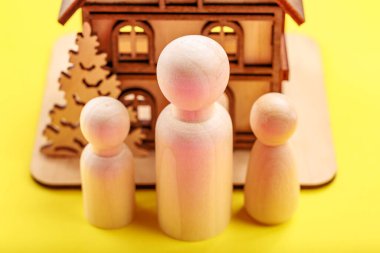 Tahta figürler, sarı arka planda minyatür evin önünde aileyi temsil ediyor..