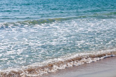 Sakin okyanus dalgaları açık mavi gökyüzünün altında yavaşça kumlu kıyıya vuruyor..