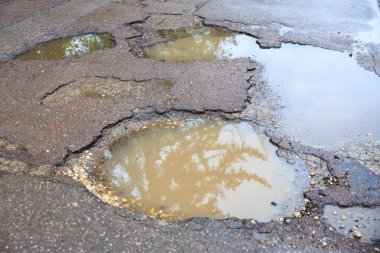 Asfalt yolda ıslak çukurlar Yağmur suyundan yansıyan yansımalarla.