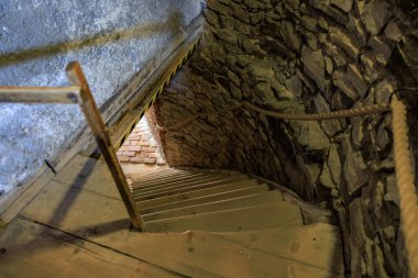 Spiral wooden staircase in ancient brick tower with stone walls.
