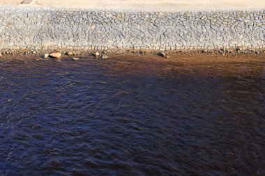 Kayalık bir kıyı şeridi olan bir su kütlesi. Su karanlık ve bulanık. Kayalar suyun her tarafına dağılmış ve suda bazı kuşlar var.