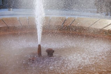 Yuvarlak çeşme suyu güneş ışığında taştan kenar püskürtür, doğal gayzerler..