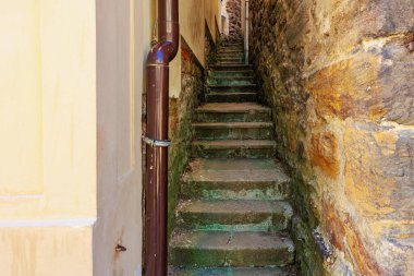 Parlak güneş ışığında tarihi binalar arasında dik adımları olan dar, taş bir ara sokak..