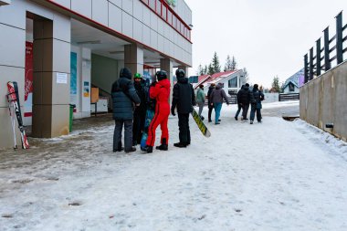 Bir grup yetişkin kış kıyafetleri içinde kayak merkezinin girişinde snowboard yapıyorlar. 15 Aralık 2024 'te Romanya.